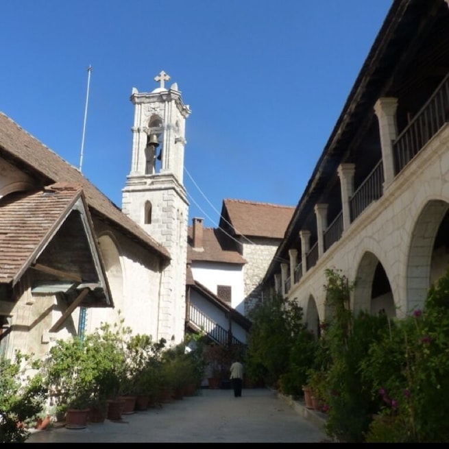 A narrow street flanked by buildings with a bell tower and arches.