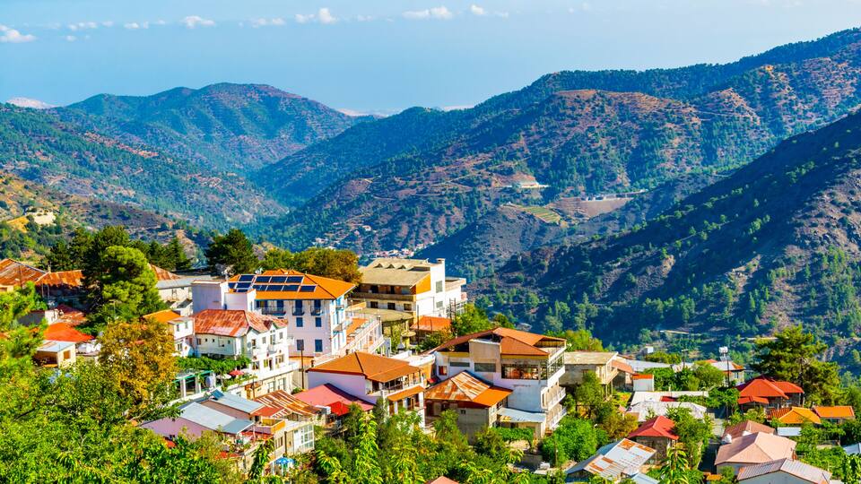 A mountainous village with terraced fields, traditional buildings with red roofs, and lush greenery.