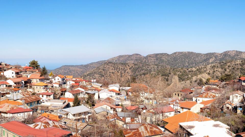 A mountainous town with red-roofed houses and a prominent white church with two domes.
