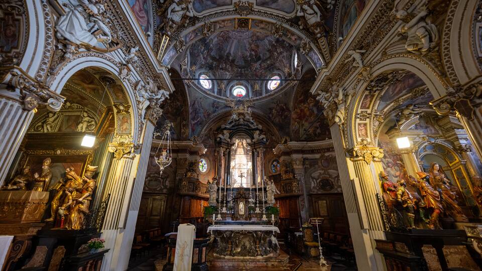 An ornate church interior with detailed frescoes, golden statues, and a central altar.