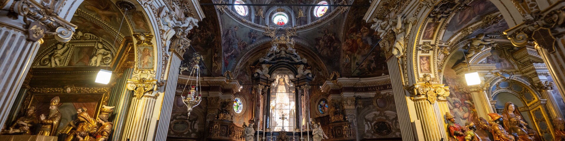 Interior de una iglesia ornamentada con frescos detallados, estatuas doradas y un altar central.