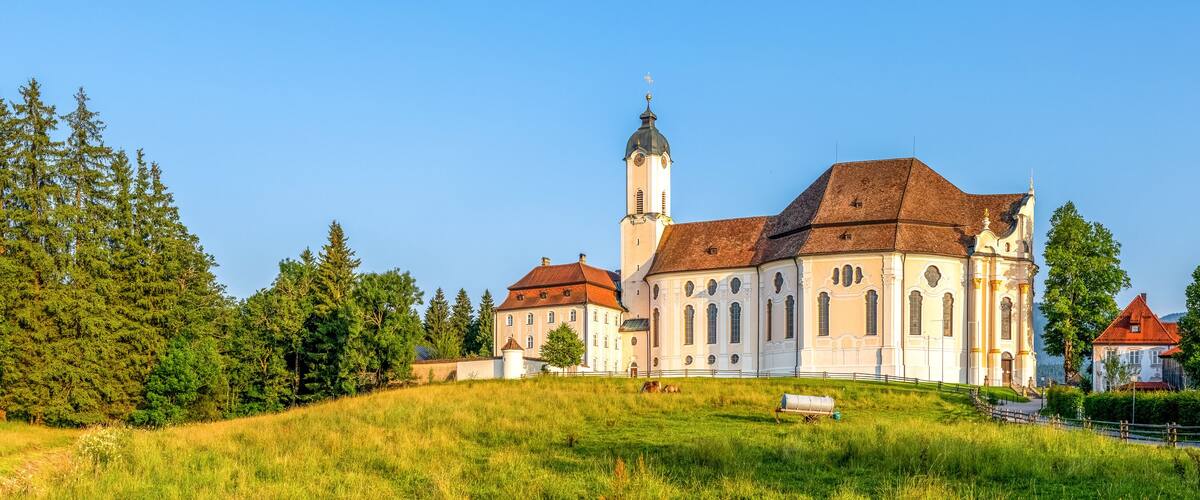 A historic church with a tall tower, surrounded by lush greenery and a hill.