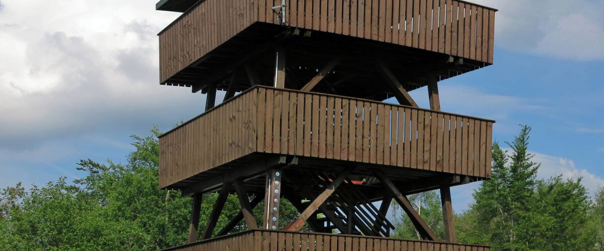 A multi-level wooden observation tower with a metal antenna, surrounded by lush greenery and trees.