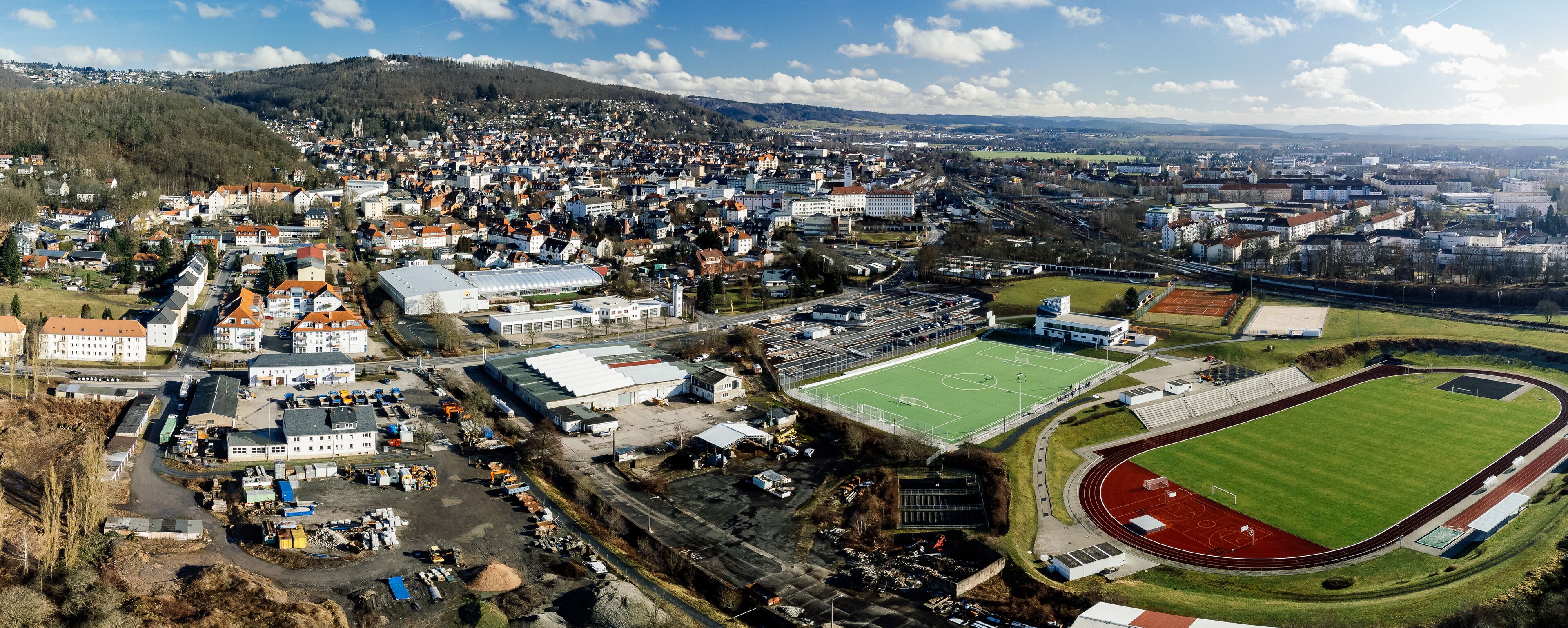 An aerial view of a town with a large stadium, a church, and surrounding residential areas.