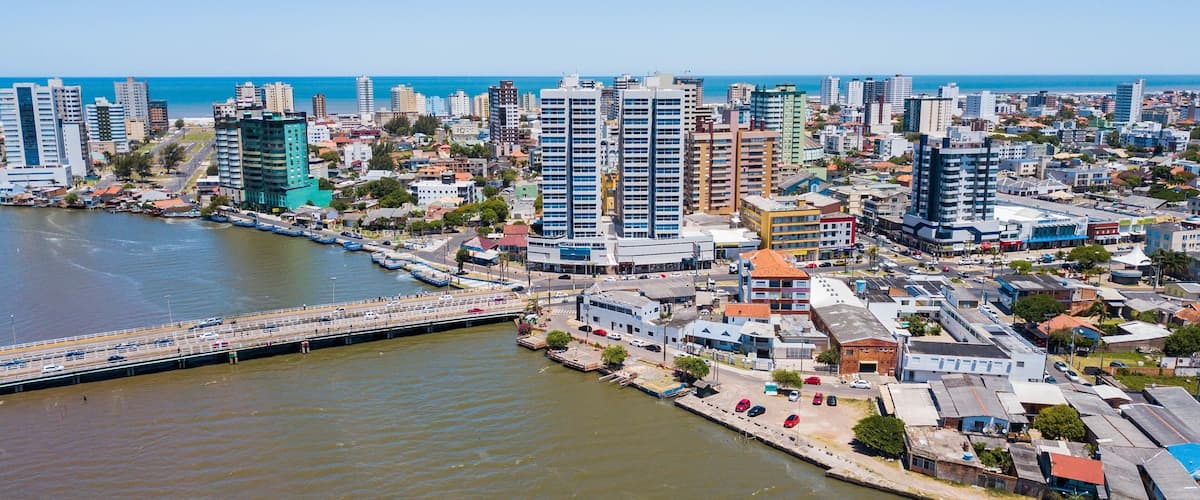 A coastal cityscape with a prominent bridge, dense urban buildings, and a clear view of the sea.