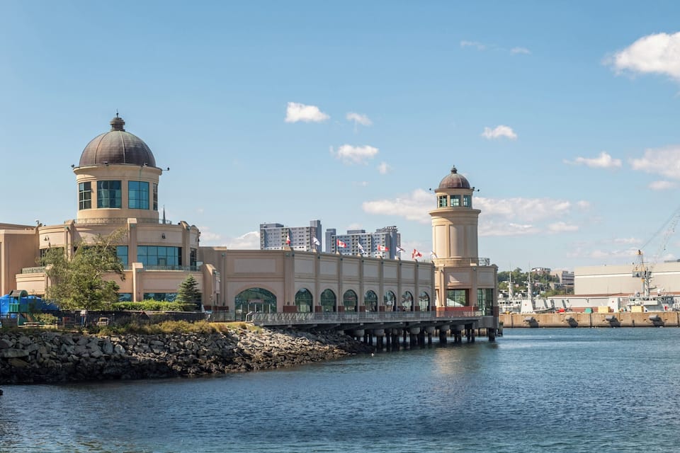 A waterfront building with two domed towers, a bridge, and a cityscape in the background.