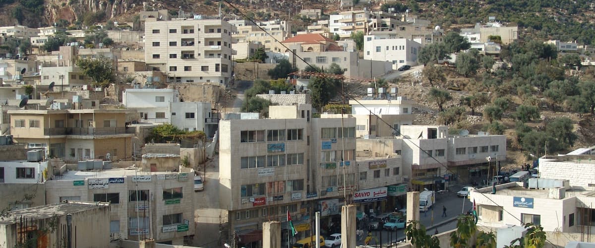 A densely built urban area with multi-story buildings, a busy street, and a hilly backdrop.