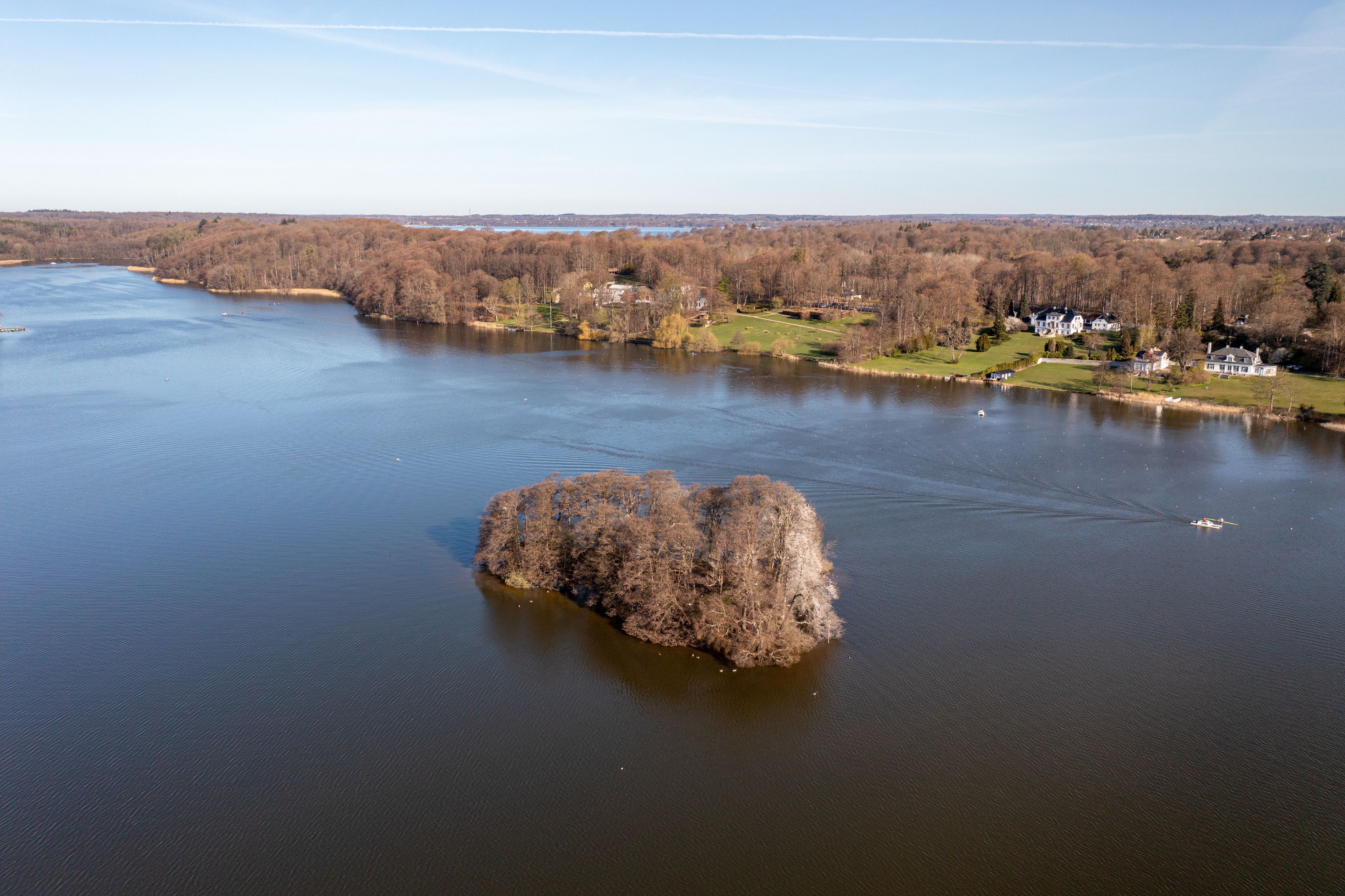 A river with a large island in the center, surrounded by trees and houses.