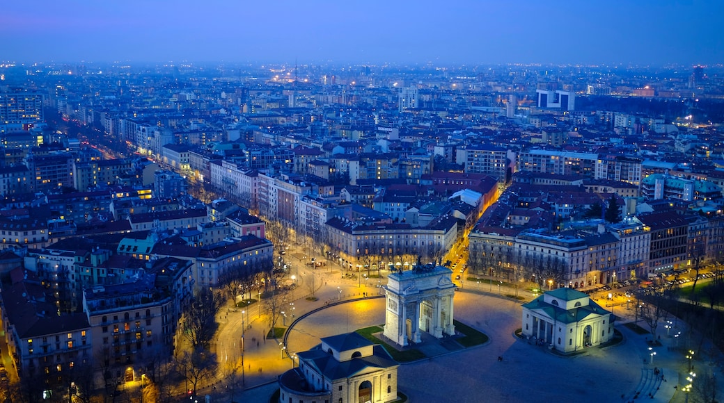 A panoramic view of a cityscape at dusk with illuminated buildings and a prominent monument in the center.