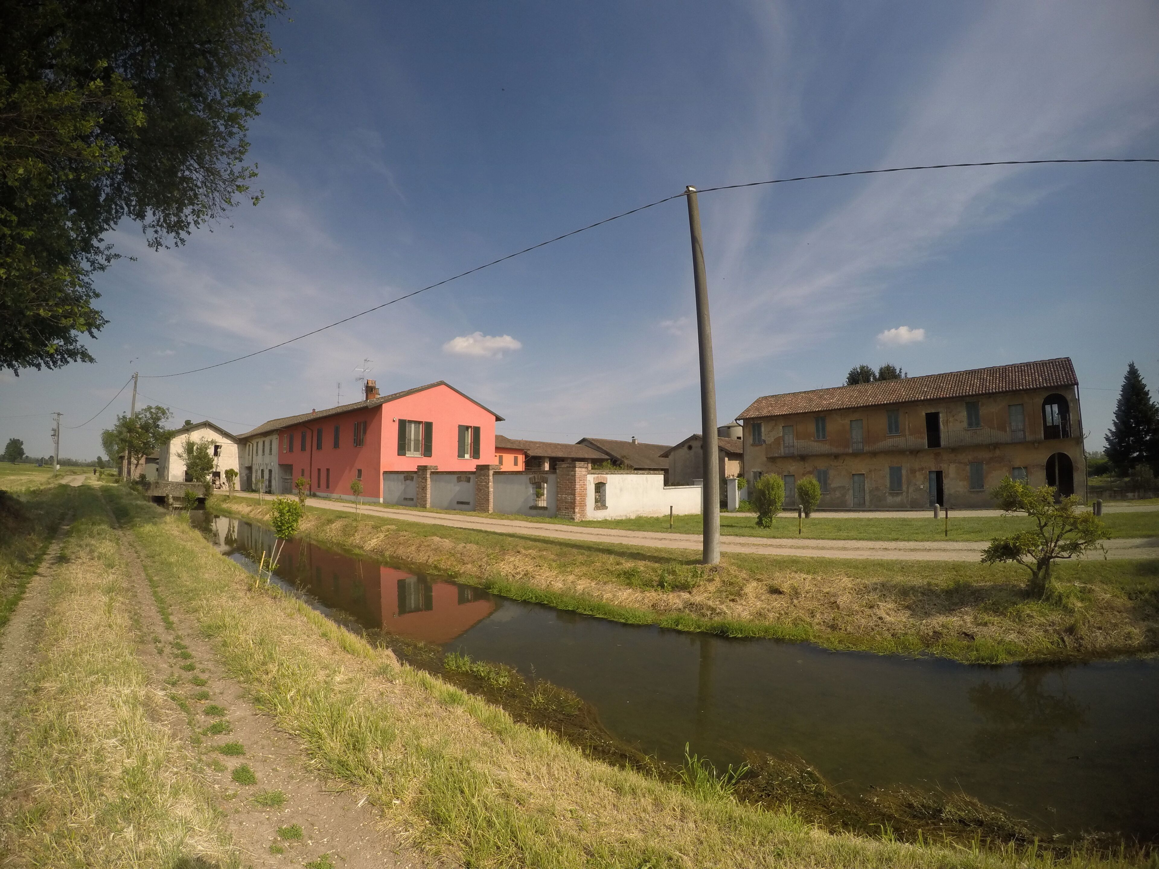 A rural landscape with a canal, a pink house, and a traditional building.
