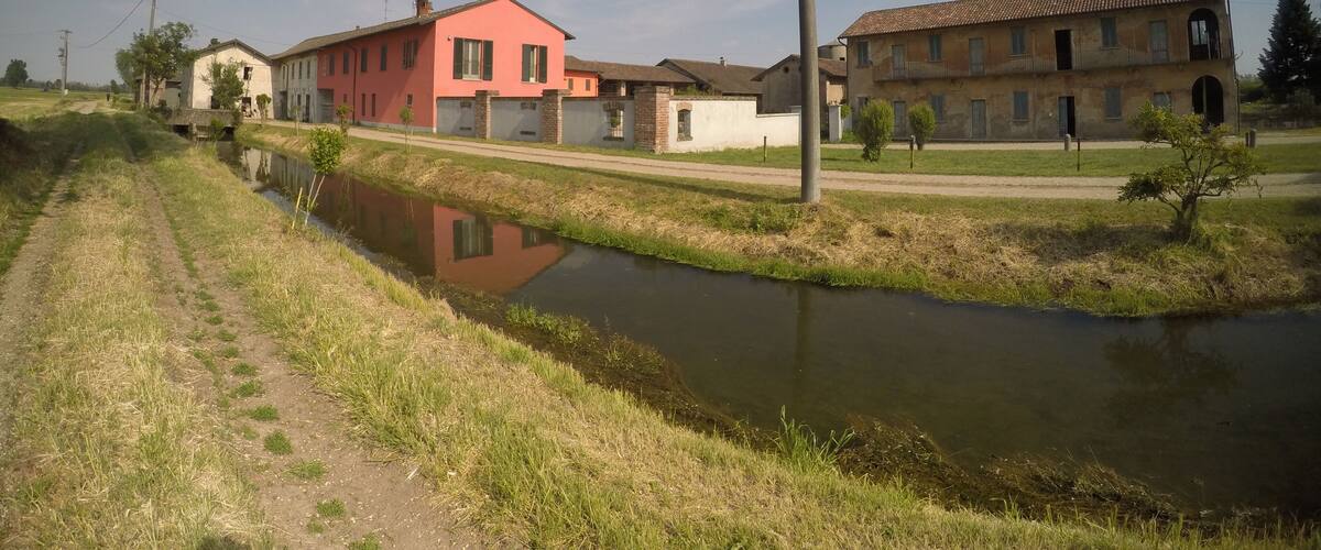 A rural landscape with a canal, a pink house, and a traditional building.
