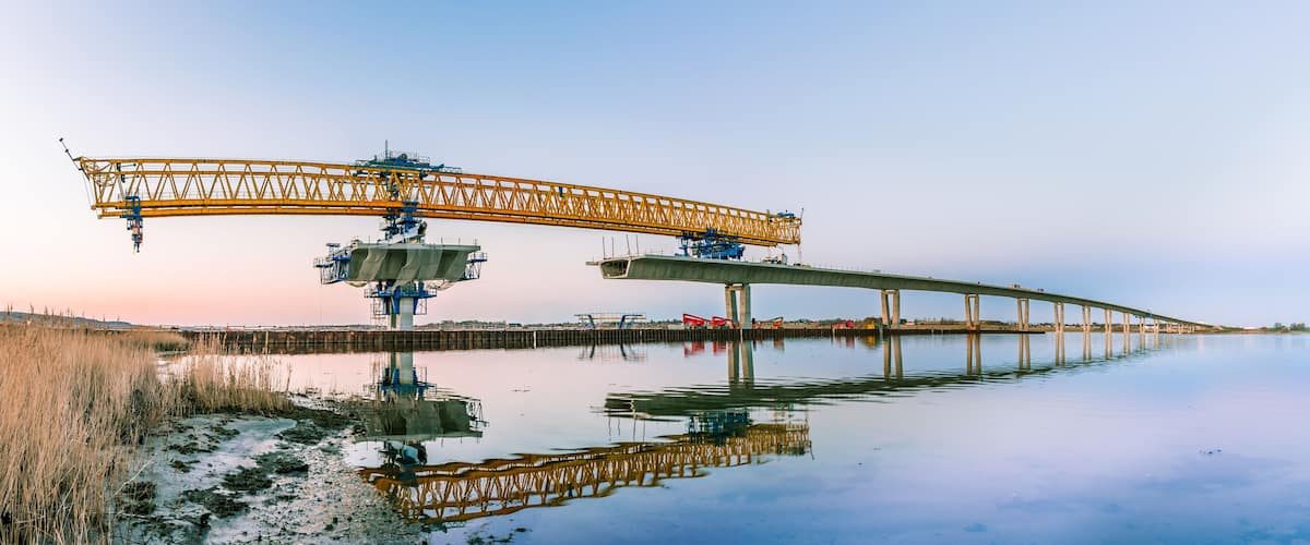 A bridge with a crane and a calm river reflecting its structure.