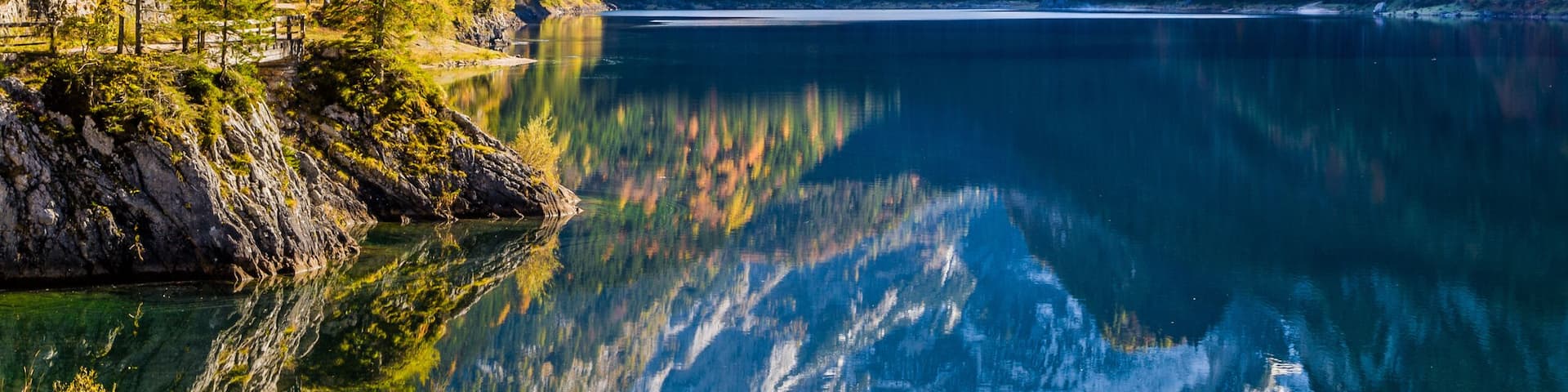 A serene lake surrounded by mountains with snow-capped peaks and autumn-colored trees.