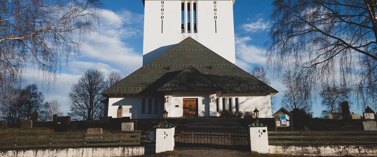 A church with a tall tower and a cross on top, surrounded by bare trees and a clear blue sky.