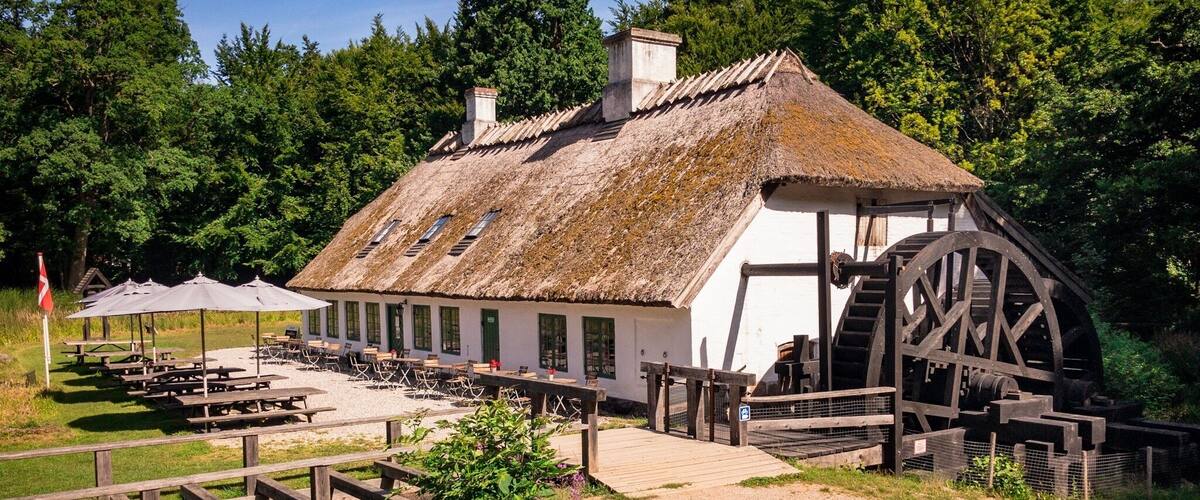 A traditional building with a water wheel, picnic tables, and a wooden deck.