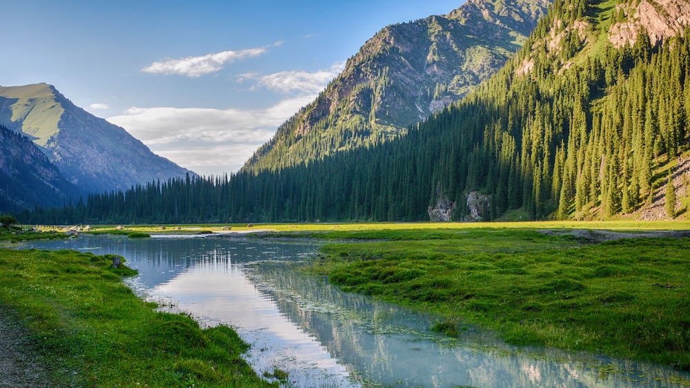Idyllic summer landscape with hiking trail in the mountains with beautiful fresh green mountain pastures, river with reflection and forest. Terskey Alatoo mountains, Tian-Shan, Karakol, Kyrgyzstan