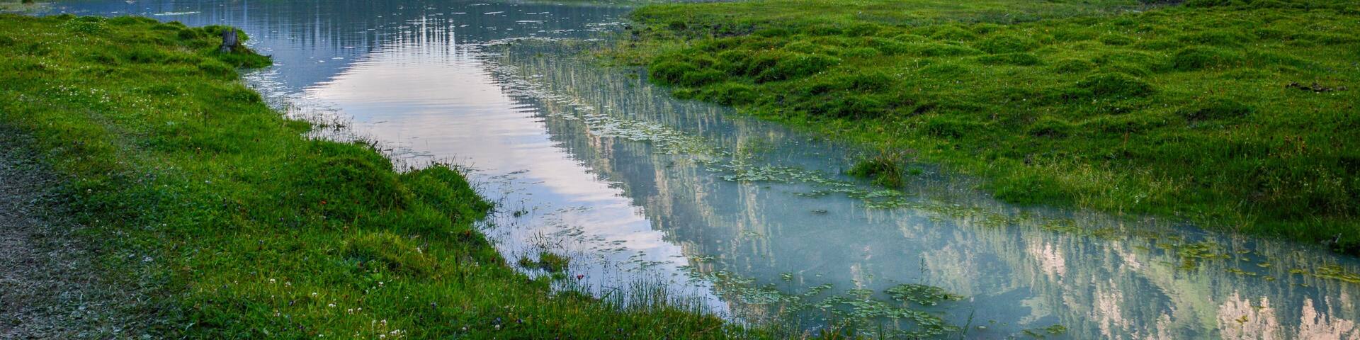 Idyllic summer landscape with hiking trail in the mountains with beautiful fresh green mountain pastures, river with reflection and forest. Terskey Alatoo mountains, Tian-Shan, Karakol, Kyrgyzstan