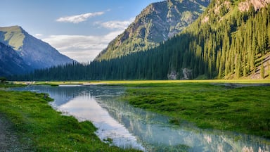 A mountain landscape with a river reflecting the greenery and a clear sky.