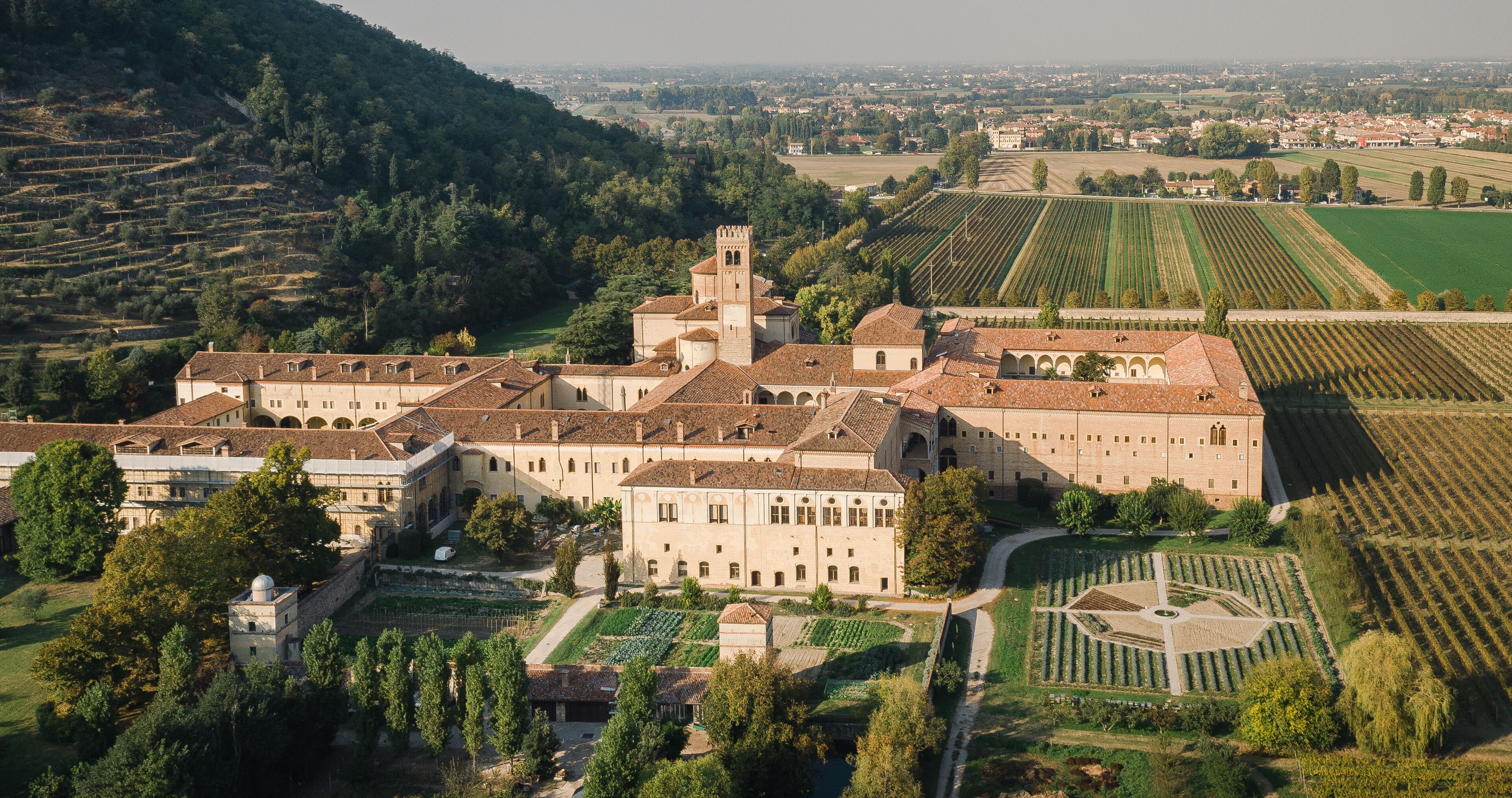A large historic building complex with a prominent tower, surrounded by terraced vineyards and lush greenery.