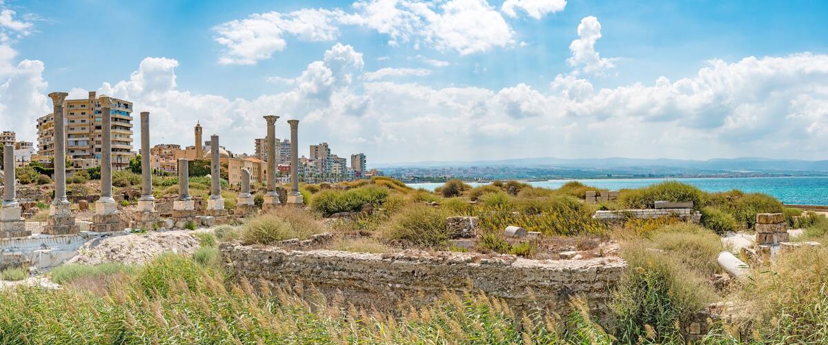 Ancient ruins with columns, a coastal view, and a clear sky.