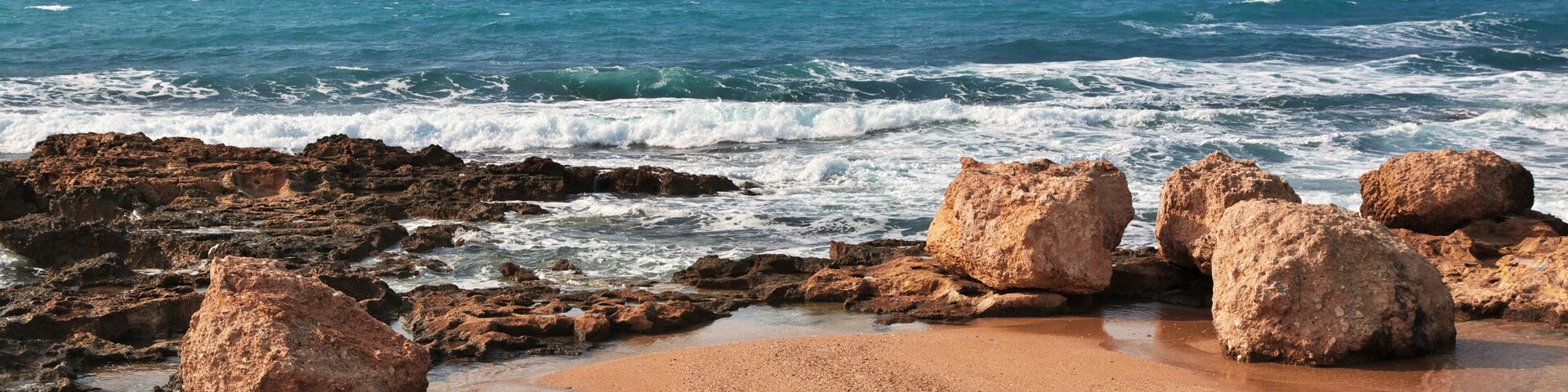 A rocky beach with waves, clear sky, and a blue flag.