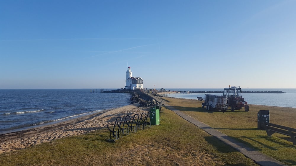 Un phare perché sur un promontoire rocheux, une plage délimitée par une clôture et un tracteur garé au bord de l’eau.