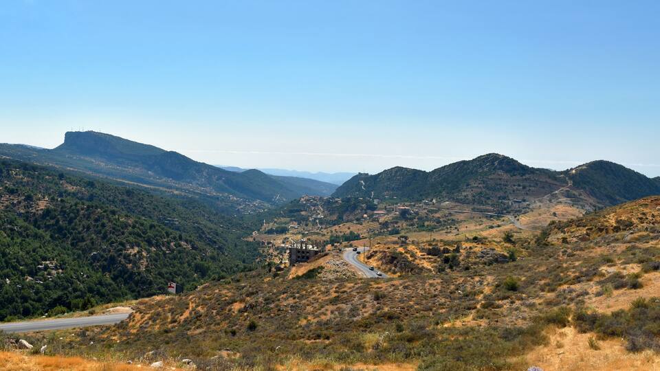 A winding road through a mountainous landscape with dense forests and rocky terrain.