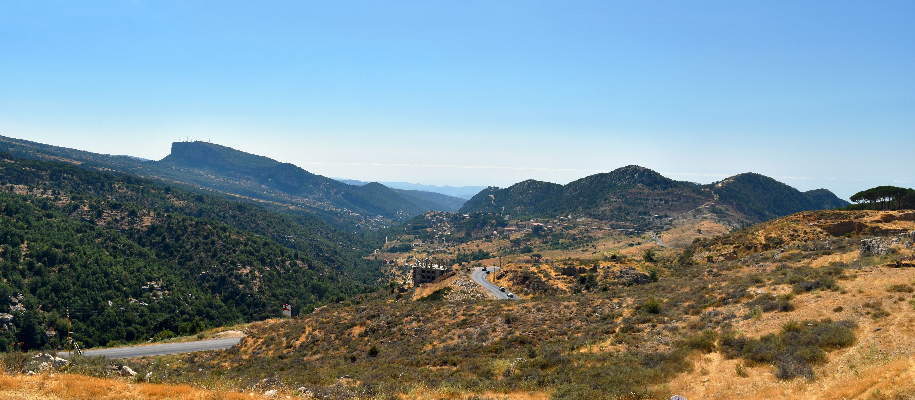 A winding road through a mountainous landscape with dense forests and rocky terrain.