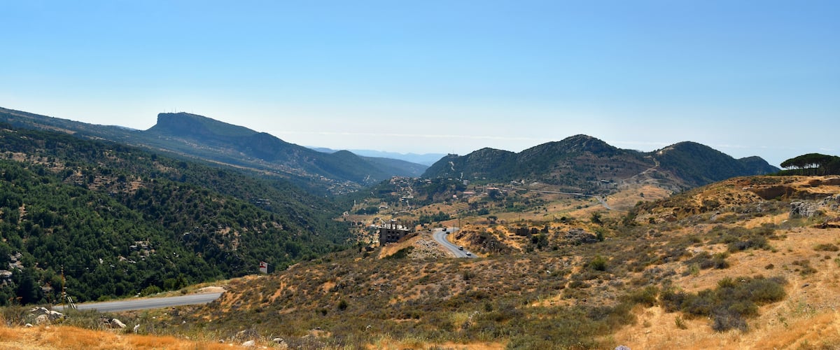A winding road through a mountainous landscape with dense forests and rocky terrain.