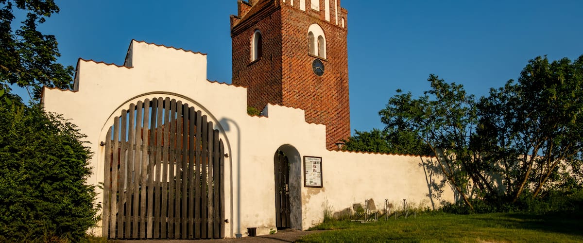 Una torre de ladrillo histórica con fachada blanca y un gran portón de arco.