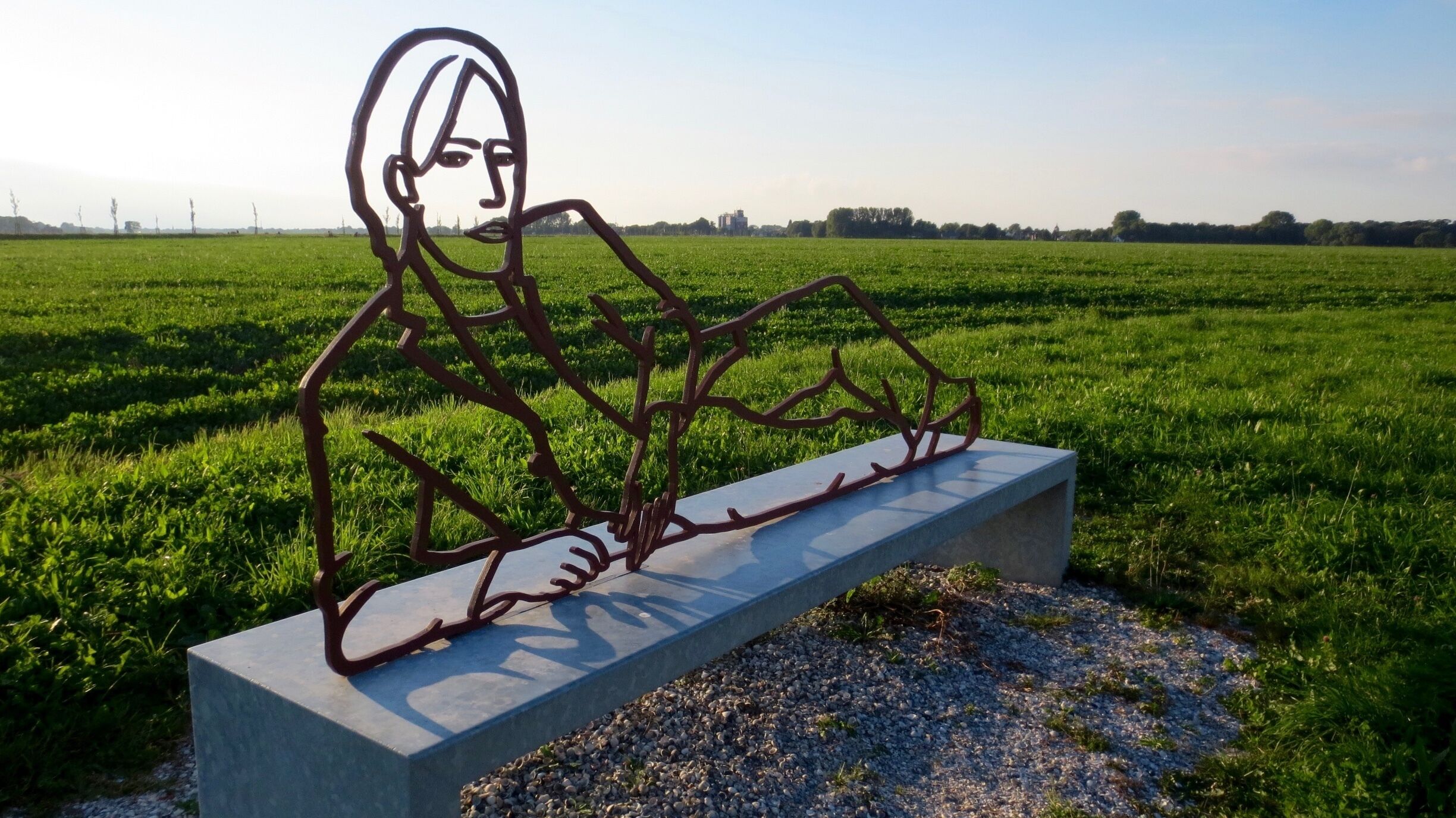 Rustpunt tussen Uithuizen en Oldenzijl.
RUSTPUNTEN – RECLINING SCULPTURES EEMSMOND
The art project Rustpunten (resting points) consists of a network of sculptures that are placed along cycling routes in the Netherlands. In beautiful places along these paths large figurative sculptures seem to have settled on a long bench. They rest or sleep in the peace and tranquility of the flat Dutch landscape. The more than life-size figurative sculptures depict contemporary people. Cut out of thick, solid steel, the figures seem to be drawn in the open space of the landscape.
http://www.staatineemsdelta.nl/project/47/rustpunten
