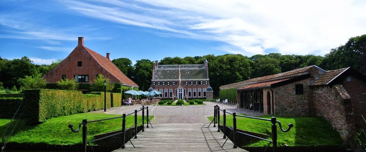 A canal with a wooden walkway leading to a large brick building with a glass roof.