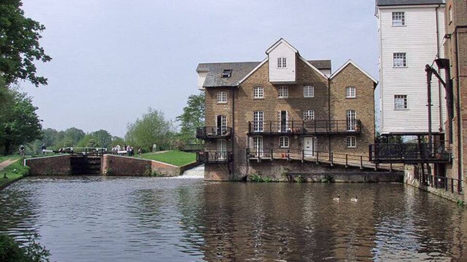 A canal with a bridge, a building with a balcony, and a white building with a chimney.