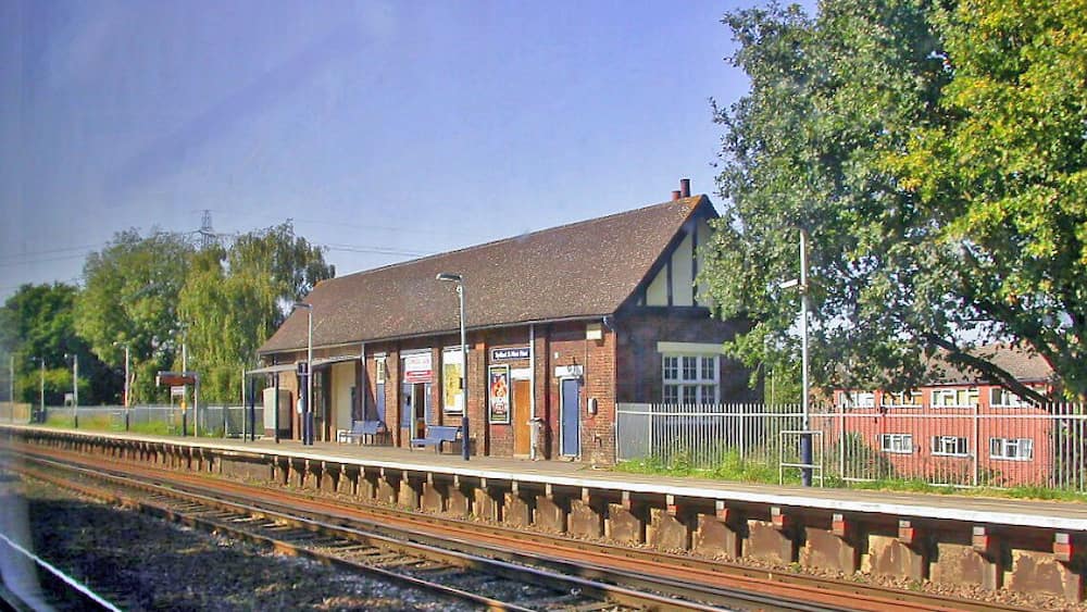 Une gare avec un quai, un bâtiment et des arbres.
