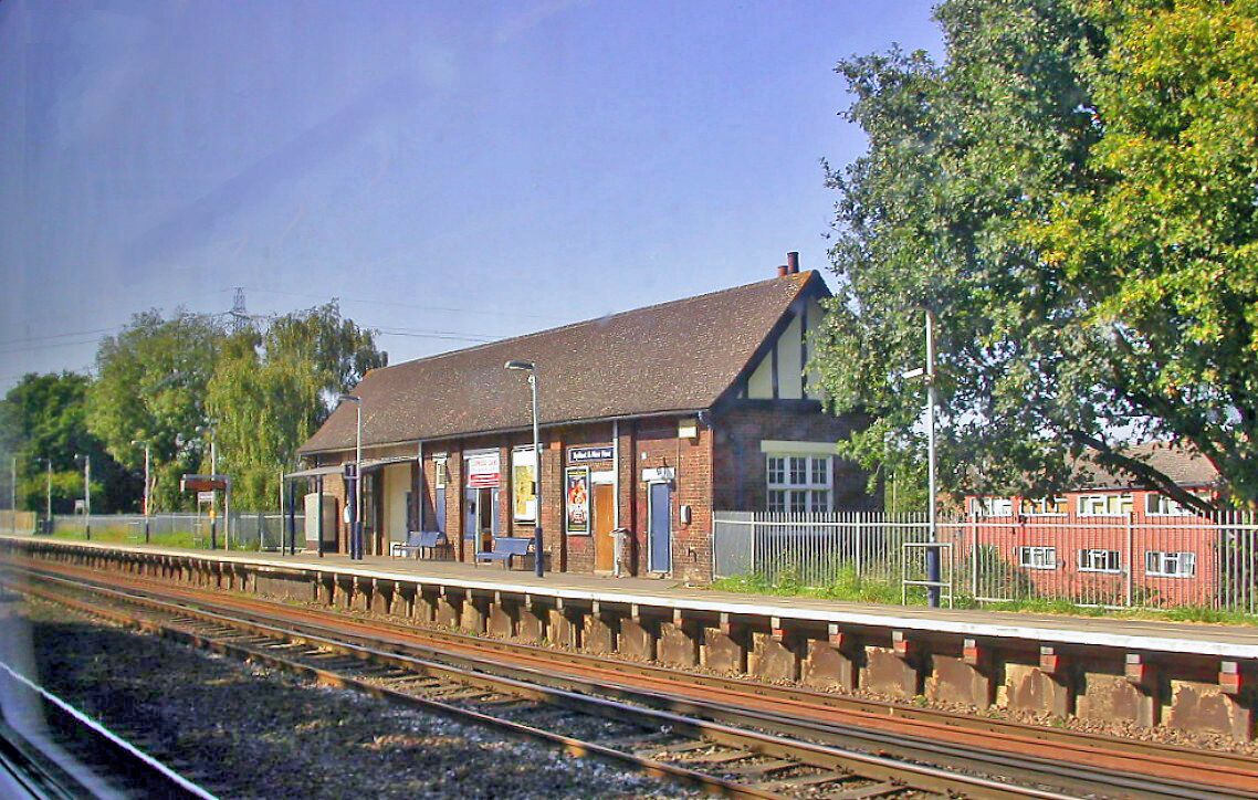A train station with a platform, a building, and trees.