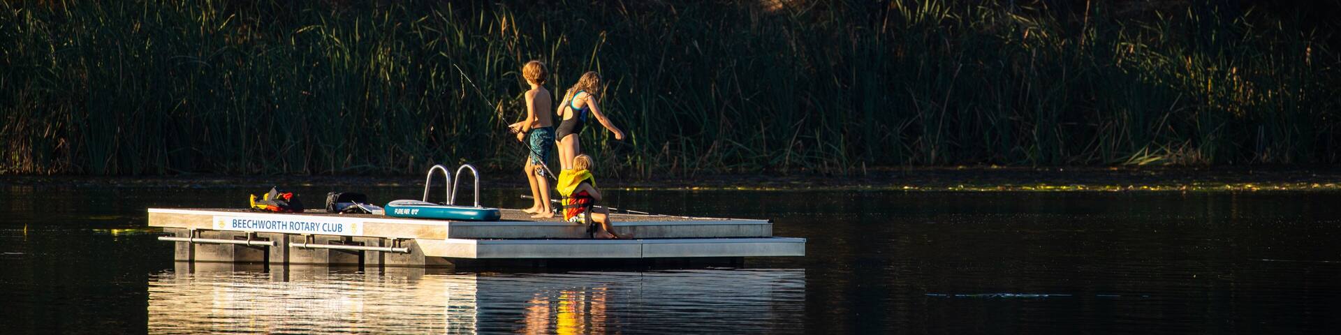A dock with a sign reading "Beechworth Rotary Club" by a calm lake surrounded by trees.