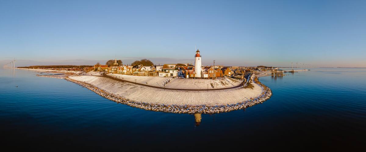 A coastal town with a prominent lighthouse, a sandy breakwater, and a calm sea.