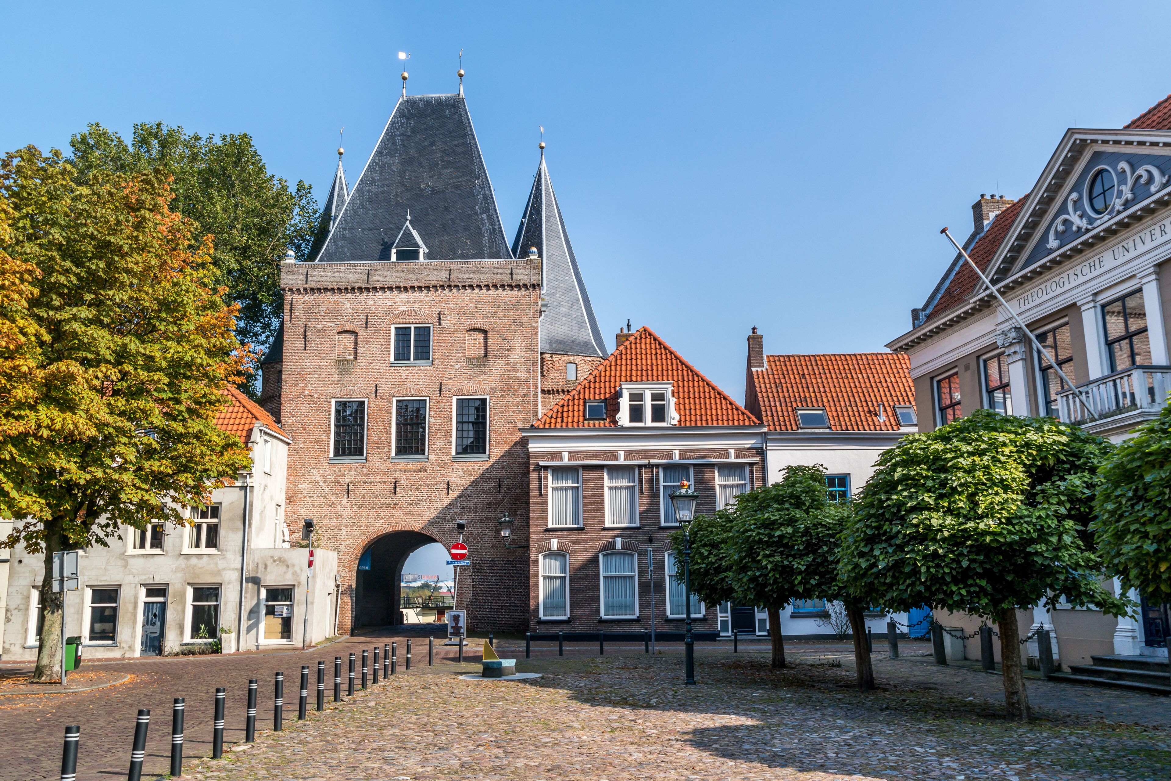 A historic building with a tower and a red-tiled roof, surrounded by cobblestone streets and trees.