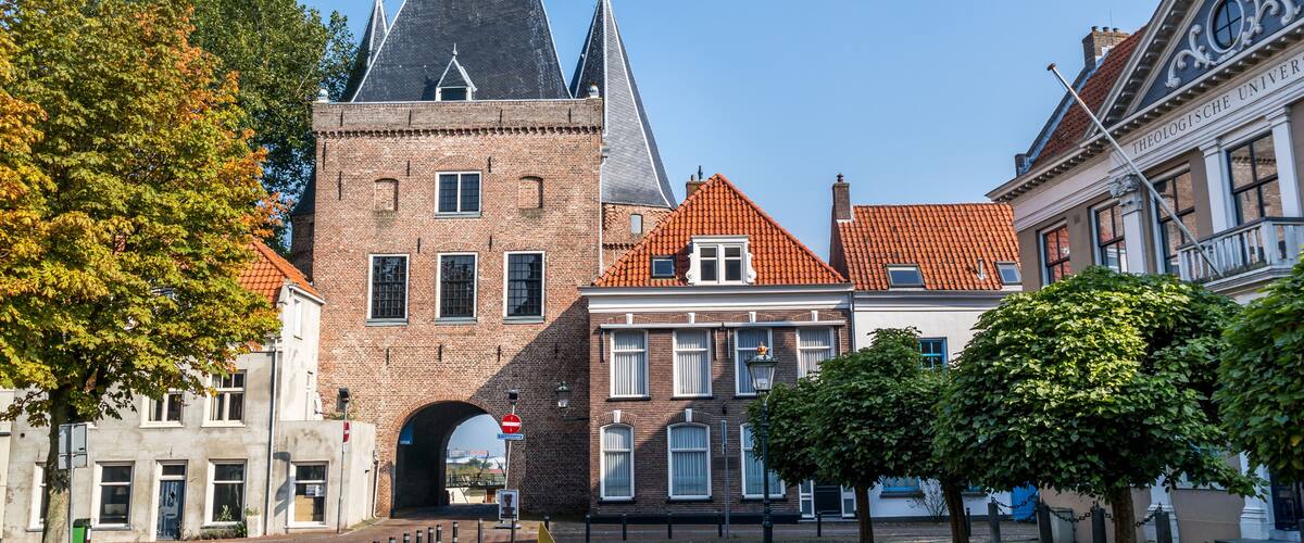 A historic building with a tower and a red-tiled roof, surrounded by cobblestone streets and trees.