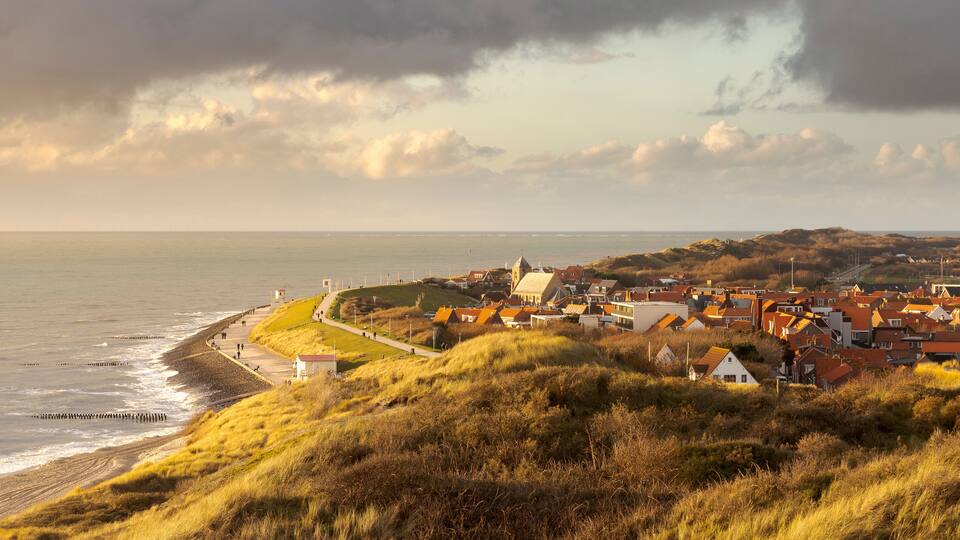 A coastal town with a beach, grassy hills, and a cloudy sky.