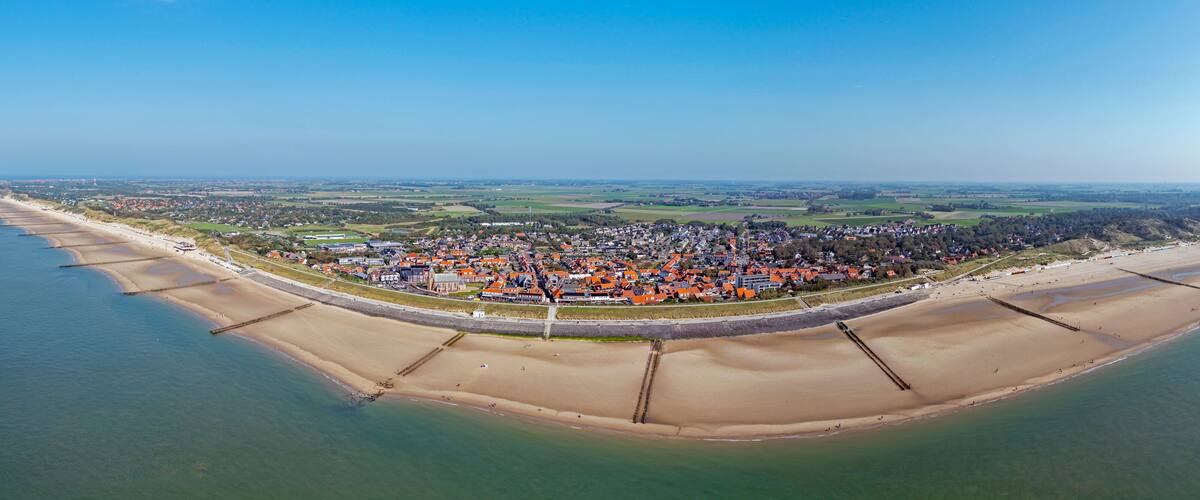 An aerial view of a coastal town with a beach, a fortified wall, and surrounding fields.