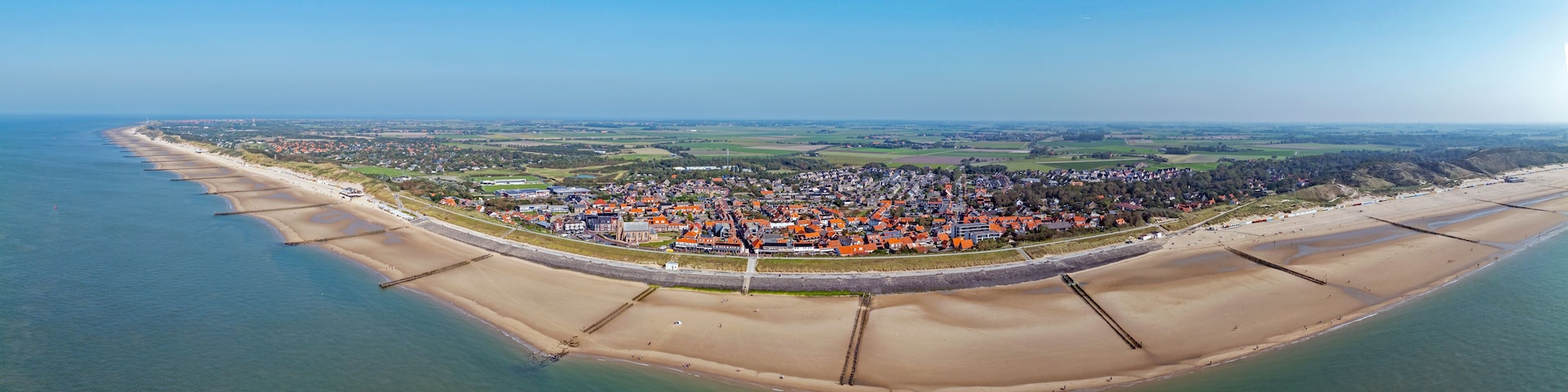 An aerial view of a coastal town with a beach, a fortified wall, and surrounding fields.
