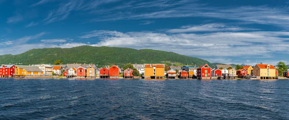 A waterfront village with colorful buildings and a forested hill in the background.