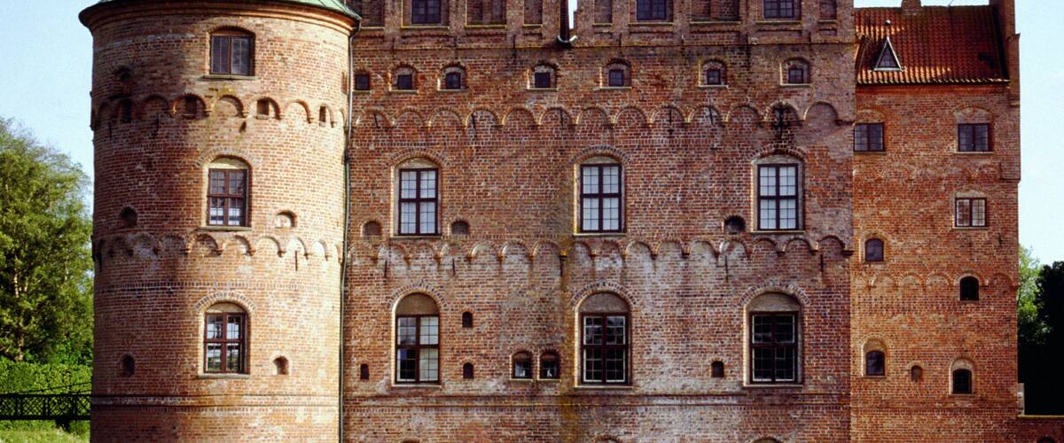 A historic castle with a round tower and multiple towers, situated by a body of water.