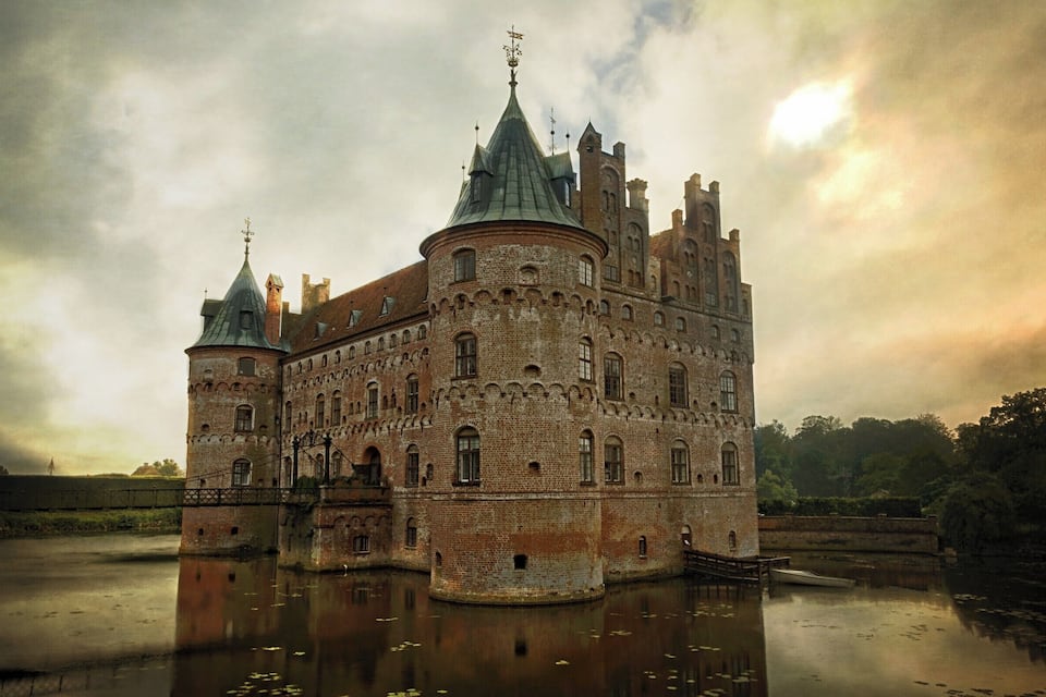 A historic castle with a moat, a bridge, and a tower.