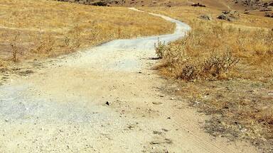 A dirt road winding through a dry, hilly landscape with sparse vegetation under a clear blue sky.