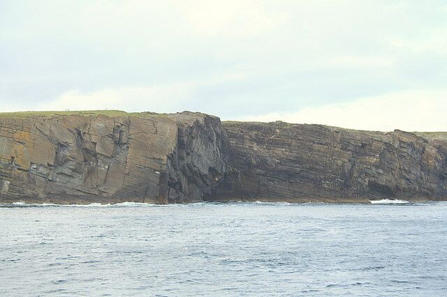 A rocky coastline with cliffs and waves crashing against them.
