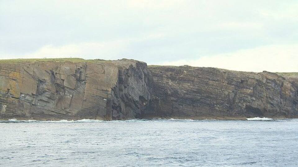 A rocky coastline with cliffs and waves crashing against them.