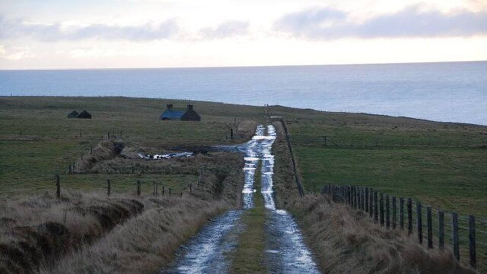 A coastal path with huts, a fence, and a grassy landscape.