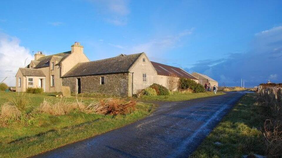 A rural road with stone buildings and a clear sky.